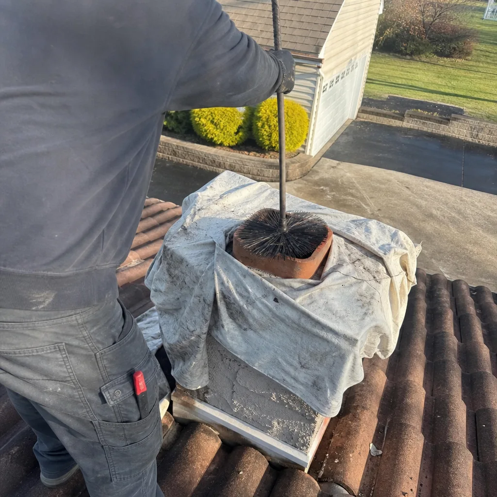 Professional chimney sweep cleaning a chimney flue with a wire brush.